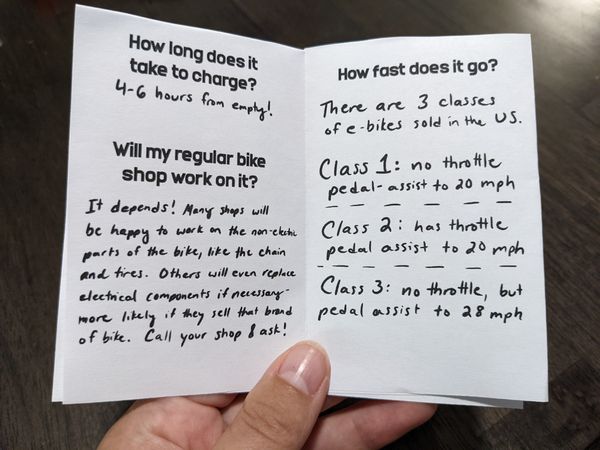 the left page of a zine reads: How long does it take to charge? 4-6 hours from empty! Will my regular bike shop work on it? It depends! Many shops will be happy to work on the non-electric parts of the bike, like the chain and tires. Others will even replace electrical components if necessary- more likely if they sell that brand of bike. Call your shop & ask! The right page reads: How fast does it go? There are 3 classes of e-bikes sold in the US. Class 1: no throttle, pedal assist to 20 mph. Class 2: has throttle, pedal assist to 20 mph. Class 3: no throttle, but pedal assist to 28 mph