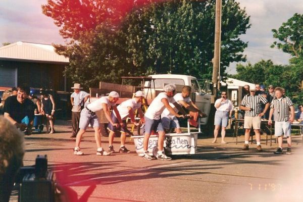 4 guys in white tee shirts carry a bathtub, getting ready to carry it while running presumably
